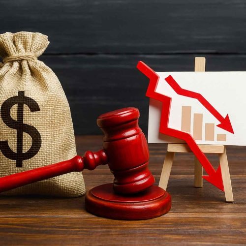 Saco de dinheiro ao lado de um martelo de juiz e um quadro com gráfico em queda, representando capital de giro afetado por juros abusivos.