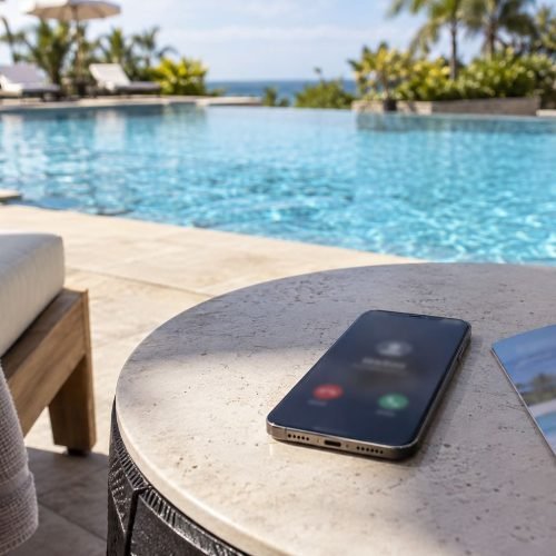 Celular sobre mesa à beira da piscina exibindo tela de chamada não atendida, borrada, ao lado de folheto dobrado